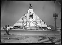 The pyramid as seen from the east side. It is surrounded by several workers and wooden beams.