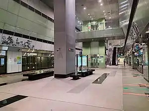 View of the underground station platform with a general grey scheme. A lift and a set of escalators in the background connects commuters from the concourse to the platforms.