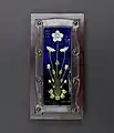 rectangular plaque with white flowers on a blue background, inset in silver