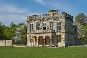 A five-bay, flat-roofed building with two storeys and an arched single-storey portico. Surrounding the top of the building is a balustrade and chimneys rise from the rear