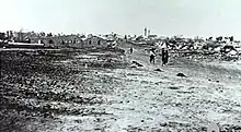 In the distance a group of people walk down a dirt road away from the village.