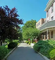An asphalt path with buildings and trees on both sides.