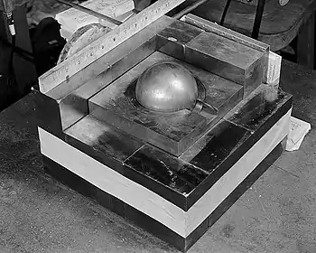 A square base of metal blocks, with a smaller square of metal on the top in the center, a Cooper block (the "core") contained in its center. A ruler along one side of the base shows it is roughly 10.5 inches (270 mm) square.