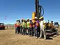 Post crew standing in front of post machine and post after its installation into the ground.