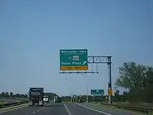 A divided highway curves to the left as the rightmost lane exits underneath an overhead green sign indicating the ramp leads to Worcester Highway and MD 589 toward Ocean Pines.